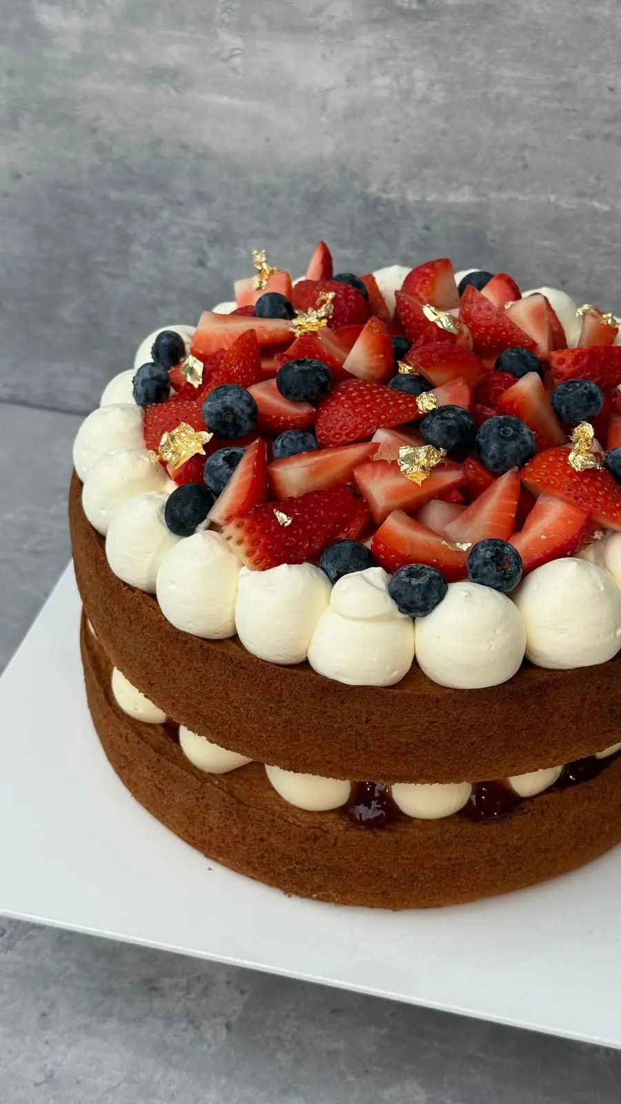 Layered chocolate cake topped with fresh strawberries, blueberries, whipped cream, and gold leaf.