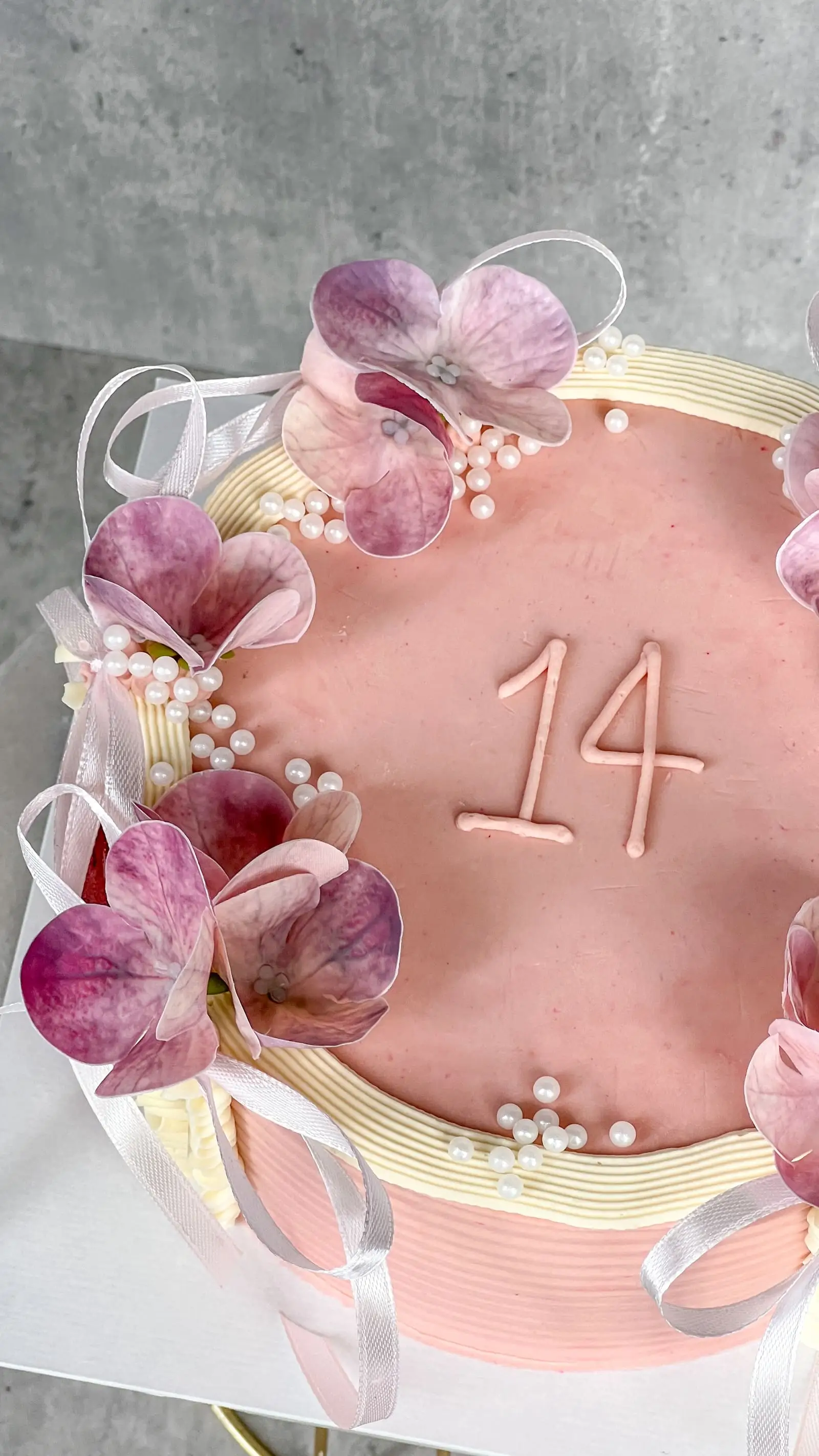 Flowery celebration cake with piped cream, edible flowers, and white ribbon detail.