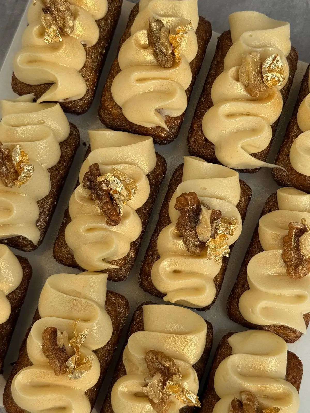 Assortment of iced chocolate cookies topped with walnuts, gold leaf, and piped cream.