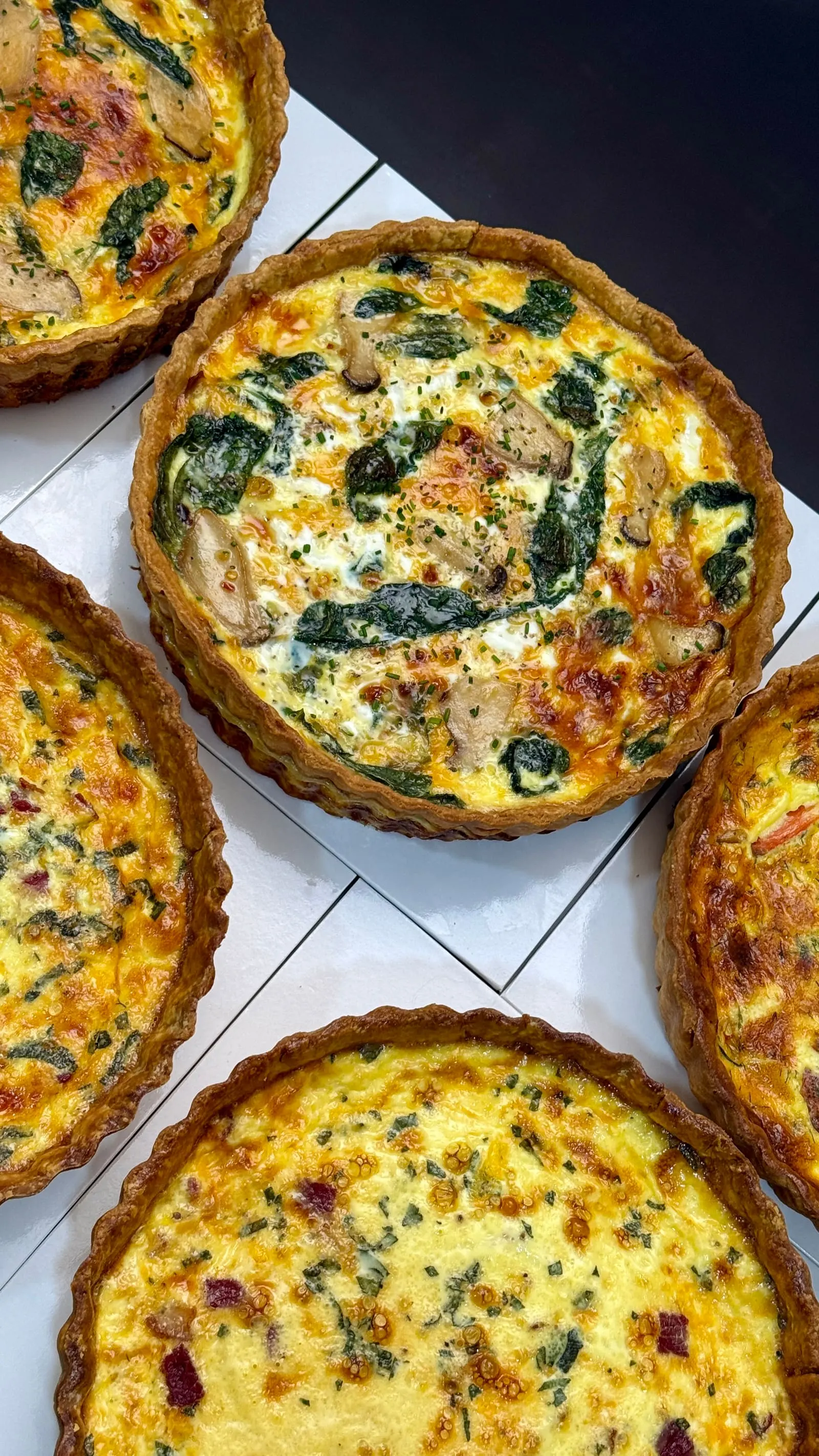 Fresh savoury quiche pastries with golden pastry crusts, spinach, mushrooms, and herbs.